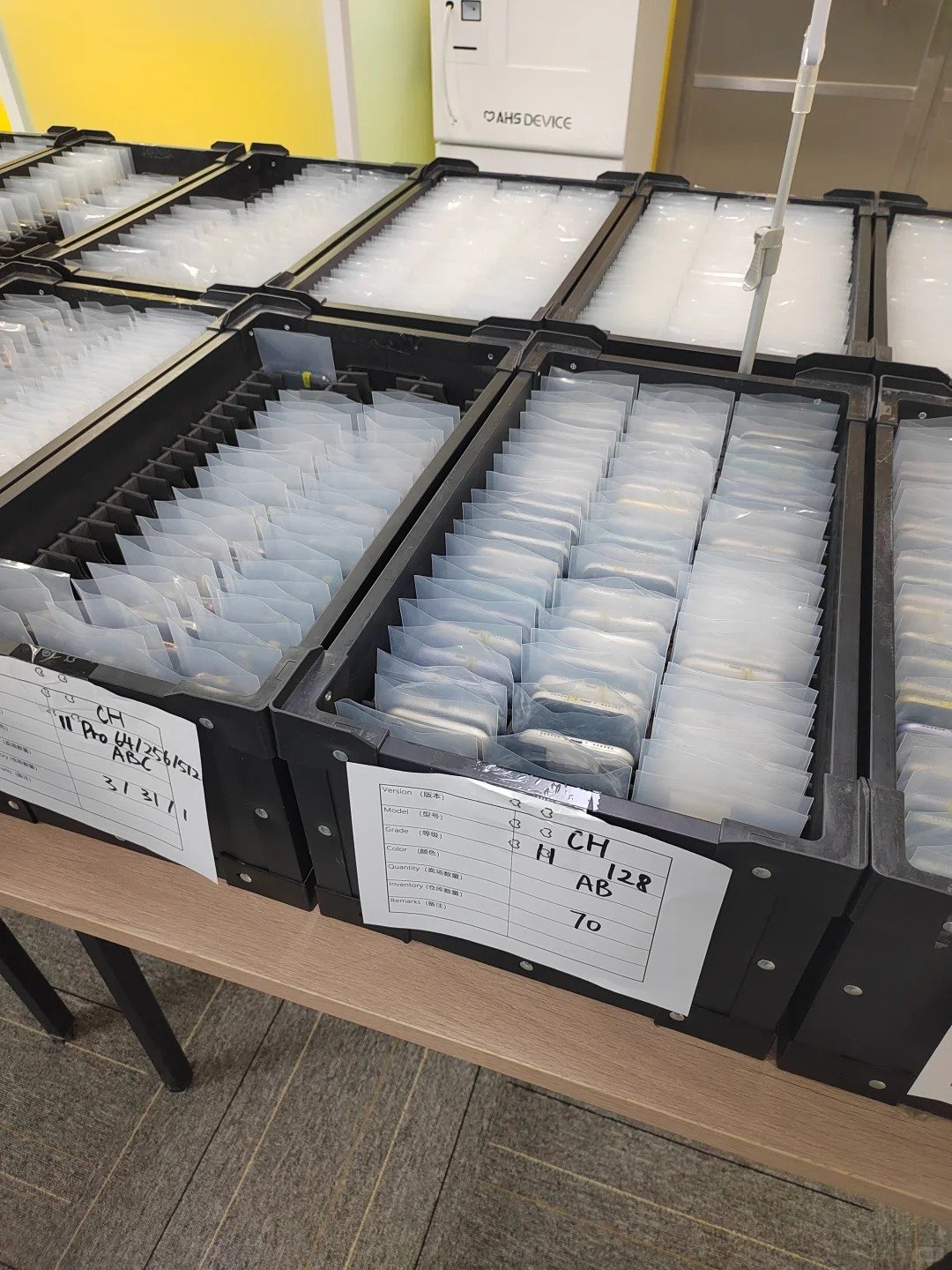 HQB receiving team reviewing a single-scene used iPhone workbench with ownership records, batch labels, setup verification notes, and quality-control documents.